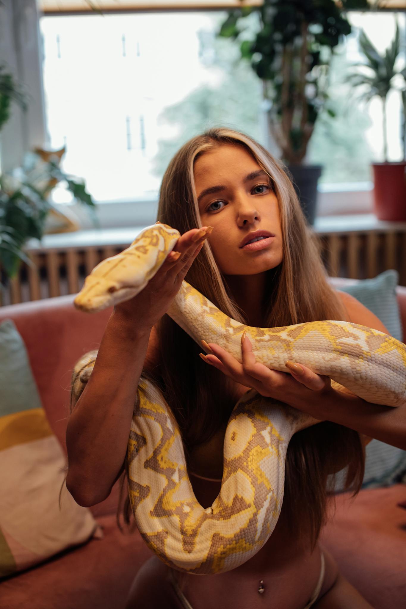 A woman with long hair holding a pet python indoors, radiating a retro vibe.